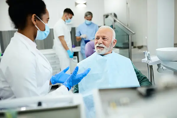 Older white patient sitting in dental chair calmly discussing his oral health with his Black female dentist at at East Portland Dentistry in Portland, OR