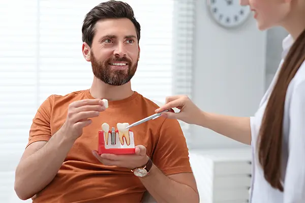 A patient holds a model of teeth with a single dental implant, while discussing types of dental implants with his dentist.